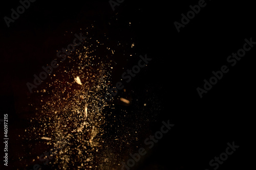 Dust and wood chips on a black background. Dirt particles fly in the air. Layout for design. Some dust particles are blurred to transmit the effect of motion.