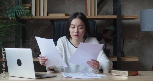 A business woman saw an error in the report while looking through business documents. The Asian woman failed to complete the task on time and closed the laptop. photo