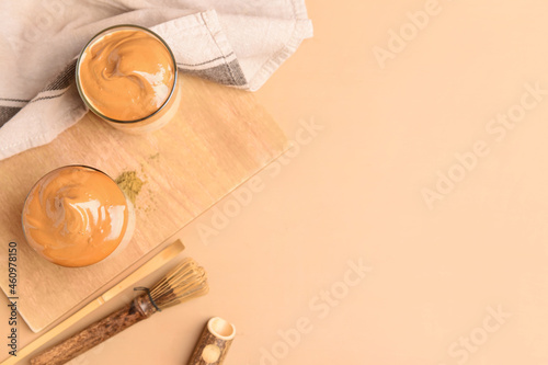 Glasses of tasty dalgona hojicha latte, chasen and chashaku on color wooden background