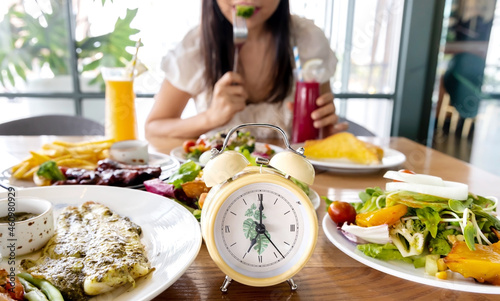 Selective focus of Alarm yellow clock  which young woman  enjoy eating of food  and Intermittent fasting diet concept in the kitchen photo