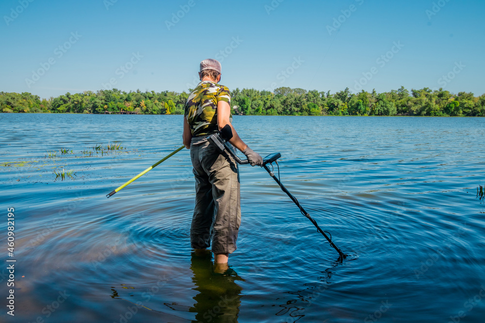 A woman in camouflage clothing searches for precious metals in the river with a metal detector. Searching for metal under water. High quality photo A woman in camouflage clothing searches for precious metals in the river with a metal detector. Searching for metal under water. High quality photo