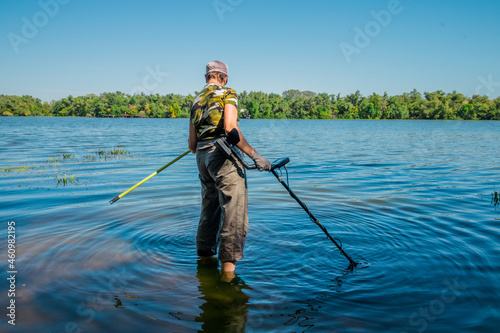  A woman in camouflage clothing searches for precious metals in the river with a metal detector. Searching for metal under water. High quality photo