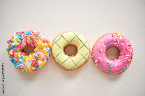 Directly above view of three multi-colored doughnuts with frosting and sprinkles against isolated background