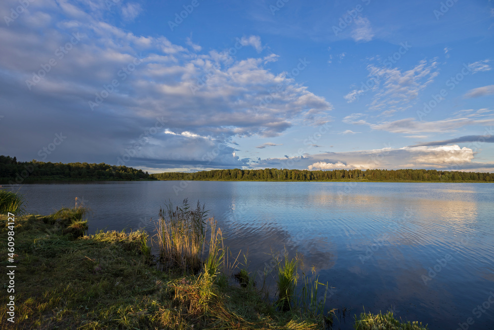 Cloudy sky over the river in the evening. Picturesque landscape with clouds and a river. Bright green grass in the foreground.