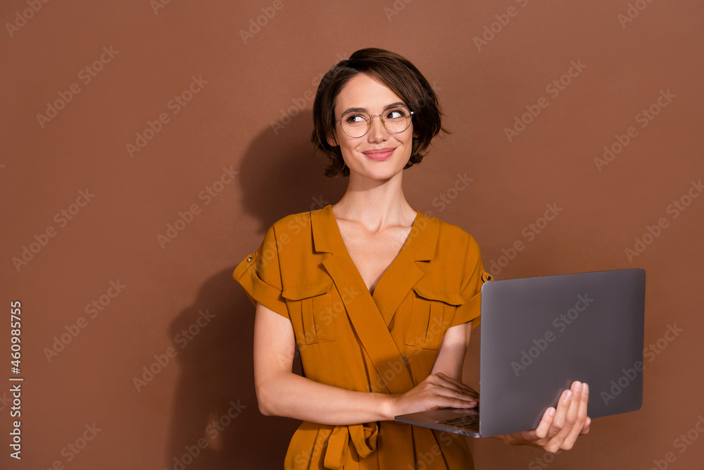 Photo of happy dreamy joyful young woman hold hands laptop wear glasses job look empty space isolated on brown color background Photo of happy dreamy joyful young woman hold hands laptop wear glasses job look empty space isolated on brown color background
