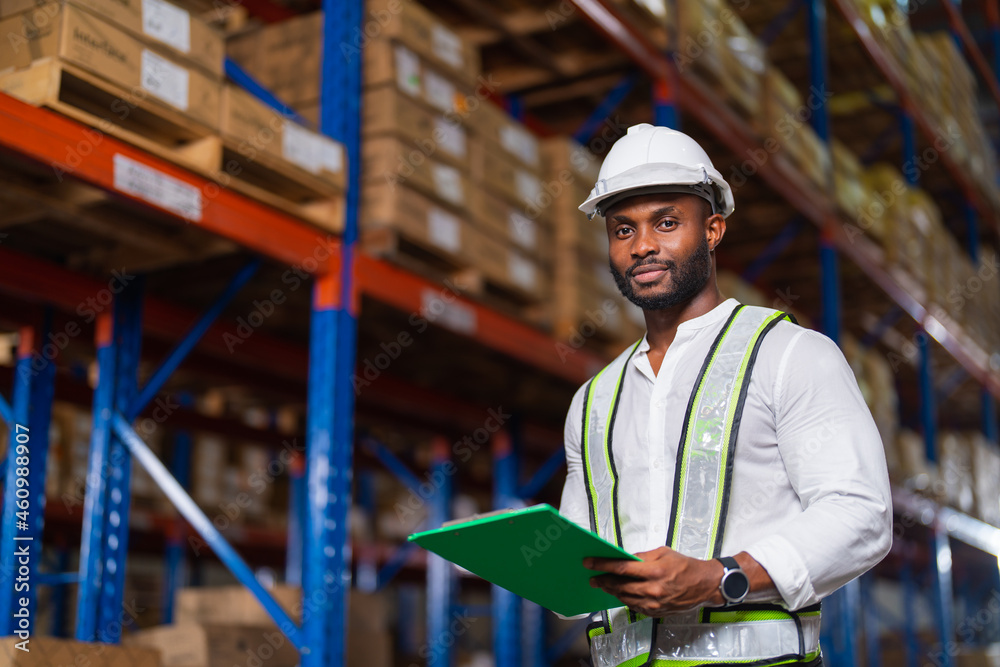 Portrait of an African warehouse manager holding a clipboard checking inventory in a large distribution center. Portrait of an African warehouse manager holding a clipboard checking inventory in a large distribution center.