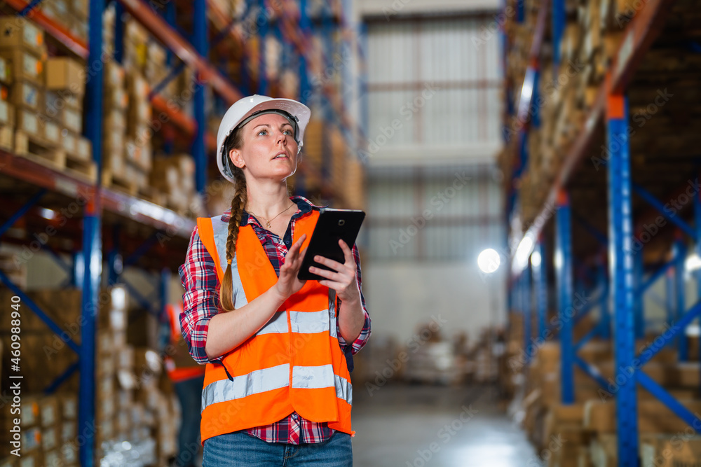 Warehouse worker working process checking the package using a tablet in a large warehouse distribution center. Caucasian female inspects cargo inventory.