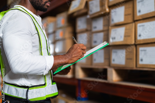 Portrait of an African warehouse manager holding a clipboard checking inventory in a large distribution center.