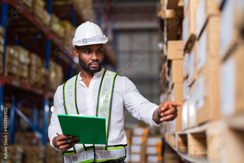Portrait of an African warehouse manager holding a clipboard checking inventory in a large distribution center.