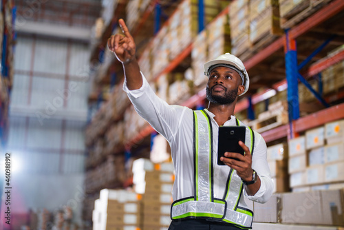 Warehouse worker working process checking the package with a tablet in a large distribution center. an African male supervisor inspects cargo delivery status.