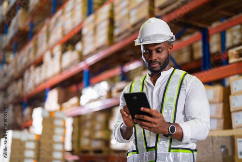 Warehouse worker working process checking the package with a tablet in a large distribution center. an African male supervisor inspects cargo delivery status.