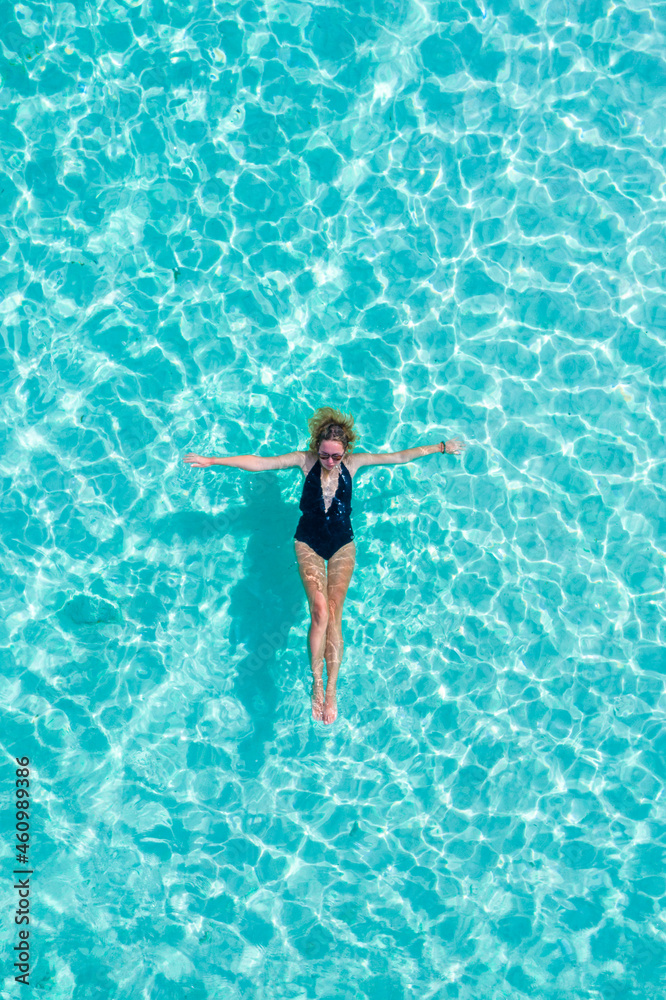 Top view aerial of a seductive sexy model in black swimwear is enjoying relax in turquoise sea summer weekend. Tropical background with empty space.