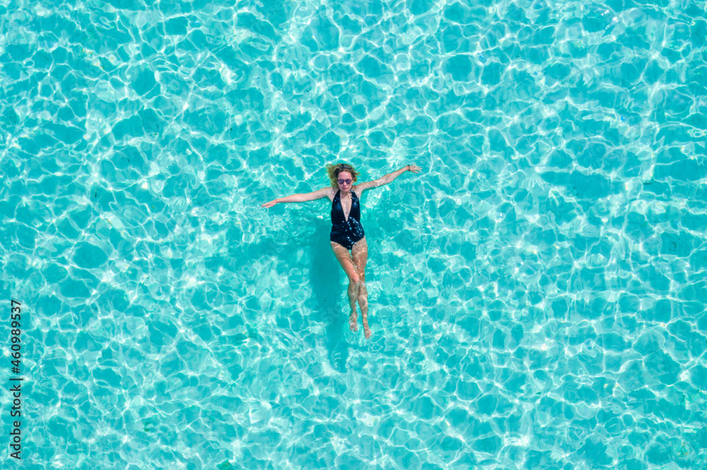 Top view aerial of a seductive sexy model in black swimwear is enjoying relax in turquoise sea summer weekend. Tropical background with empty space.