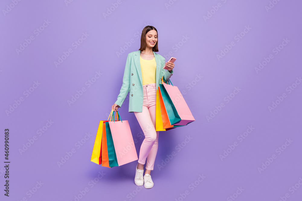 Full length photo of pretty positive lady hold store mall packages use telephone isolated on purple color background Full length photo of pretty positive lady hold store mall packages use telephone isolated on purple color background