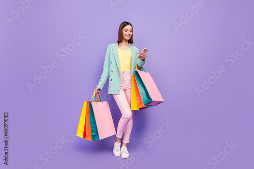 Full length photo of pretty positive lady hold store mall packages use telephone isolated on purple color background