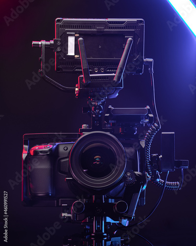 Professional videographer equipment, digital camera with lens in cage. Front view on a black table background.
 photo