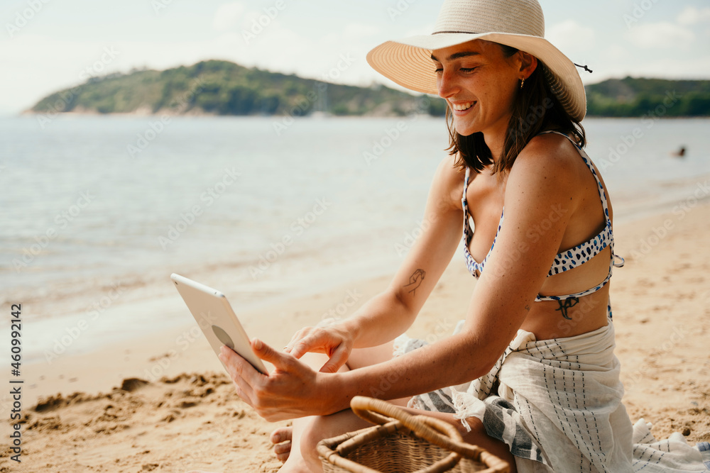 Caucasian female sun bathing on beach reading on digital tablet