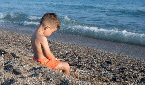 Sad child sitting alone in sandy beach near the sea