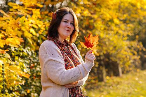 Portrait of beautiful romantic young woman with autumn yellow brown and red leaves  cute stylish girl in park holding golden leaves  Selective focus  natural light  vibrant colors  body positivity