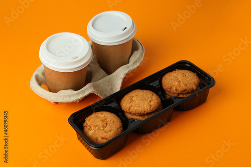 Cookies and paper cups of coffee on orange background