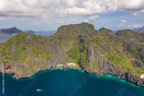 Aerial drone view of boats over a tropical coral reef and remote sandy Hidden Beach, El Nido, Palawan, Philippines.