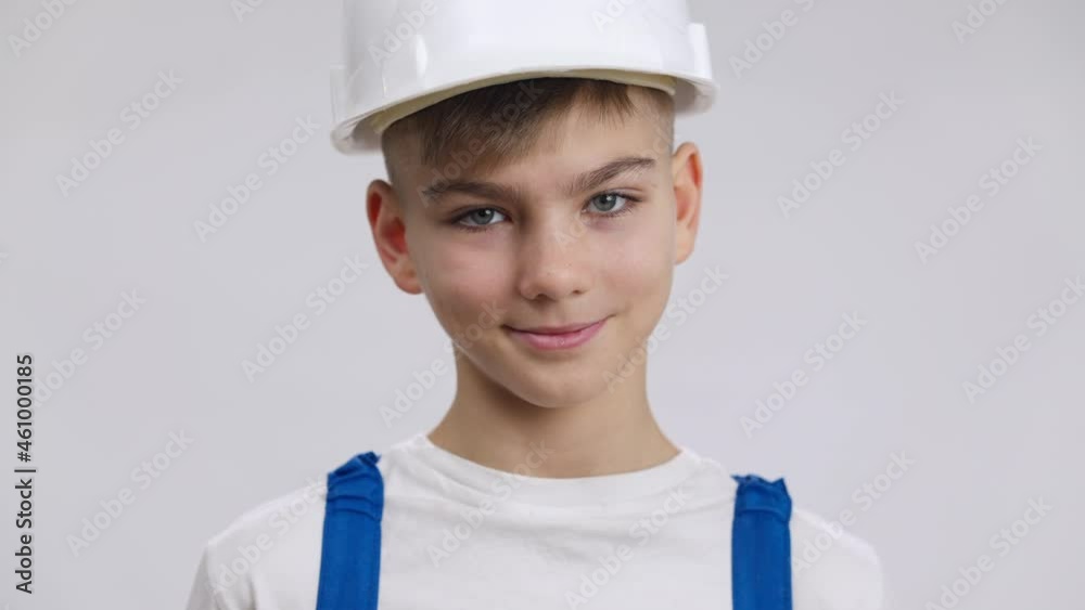 Close-up portrait of handsome Caucasian boy in hard hat posing at white background. Happy cute kid in builder uniform looking at camera smiling. Profession choice and decision-making Close-up portrait of handsome Caucasian boy in hard hat posing at white background. Happy cute kid in builder uniform looking at camera smiling. Profession choice and decision-making