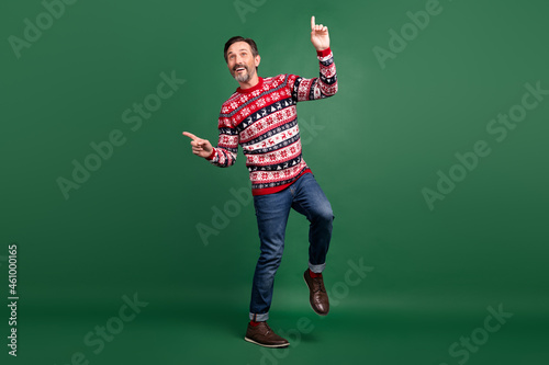 Full body photo of positive cheerful man point finger empty space dance isolated on green color background