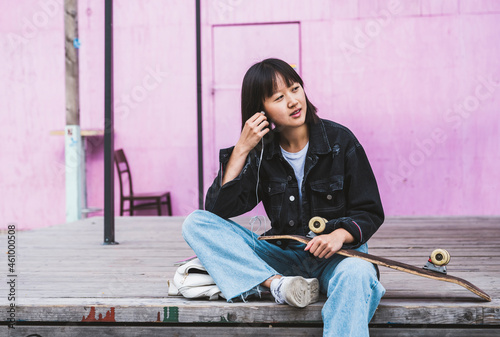 Female teenager with skateboard listening music through in-ear headphones photo