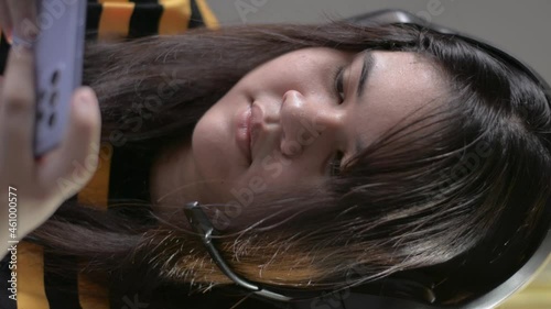 Vertical portrait Asian chubby serious girl playing online games and chatting to friends with headset on mobile smartphone at home. Close up cute plump female teenager lifestyle.