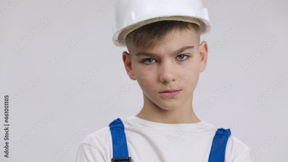 Close-up unhappy Caucasian boy looking at camera with dissatisfied facial expression posing at white background in builder uniform. Portrait of sad handsome cute kid unsure in profession choice Close-up unhappy Caucasian boy looking at camera with dissatisfied facial expression posing at white background in builder uniform. Portrait of sad handsome cute kid unsure in profession choice