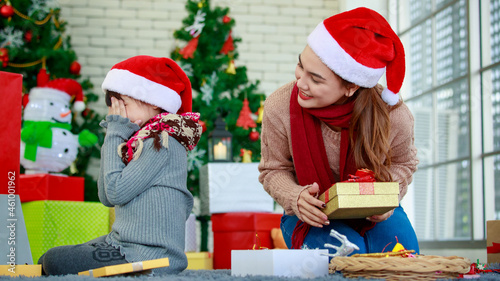 Attractive Asian mother and daughter wearing winter outfits and Santa's hat unboxing gifts celebrating Christmas with joy. Decorated Christmas tree background. Concept for family Christmas party