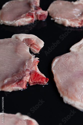 Raw pork chops on black baking tray seasoned with oil and ready for barbecue