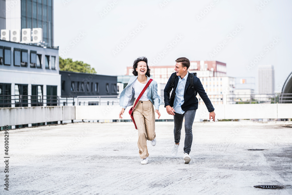 Cheerful male and female business colleagues running on rooftop Cheerful male and female business colleagues running on rooftop