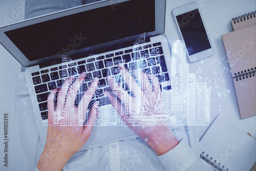 Double exposure of woman hands working on computer and buildings construction hologram drawing. Top View. smart city concept. photo