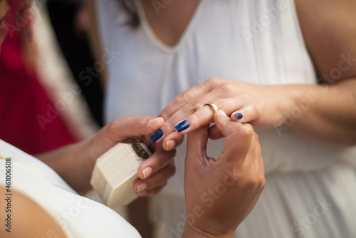 Close-up of woman putting engagement ring on her bride finger. Woman in wedding dress holding hand. Wedding  LGBT  celebration concept