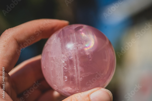 closeup of hand holding a rose quartz sphere with a rainbow