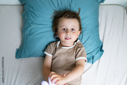 Close up portrait of a child lying in a bed in the morning. Adorable toddler wearing pajamas waking up and playing, view from above. Easy awakening concept.