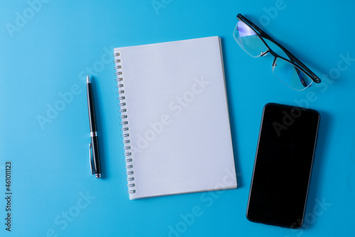 Top view of blank open notebook on blue background and different objects. Minimal flat lay style.