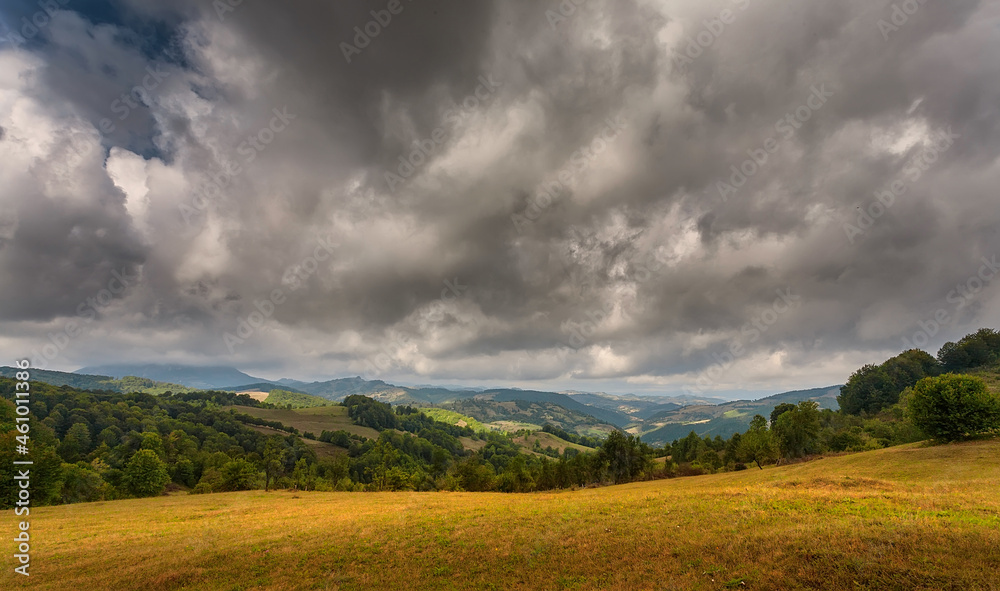 Autumn mountain landscape - yellowed and reddened autumn trees combined with green needles and blue skies. Colorful autumn landscape scene in the Romanian Carpathians. Panoramic view.