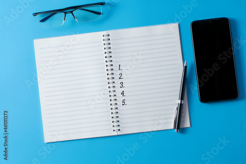Top view of blank open notebook on blue background and different objects. Minimal flat lay style.
