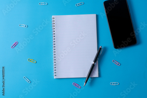 Top view of blank open notebook on blue background and different objects. Minimal flat lay style.