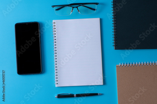 Top view of blank open notebook on blue background and different objects. Minimal flat lay style.