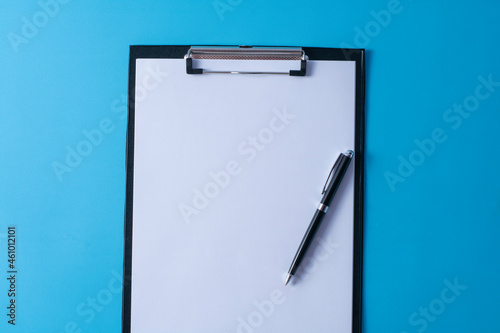 Top view of blank paper on clipboard on blue background and different objects. Minimal flat lay style.