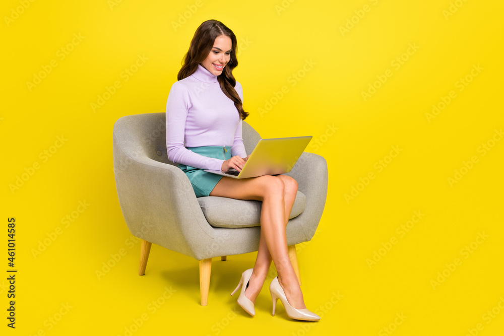 Full body portrait of charming curly hairstyle positive lady sit on chair use wireless netbook isolated on yellow color background Full body portrait of charming curly hairstyle positive lady sit on chair use wireless netbook isolated on yellow color background