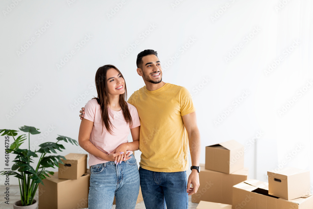 Happy young multiracial couple standing in their house among cardboard boxes on moving day, copy space Happy young multiracial couple standing in their house among cardboard boxes on moving day, copy space