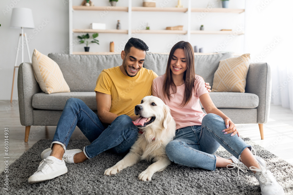Full length portrait of cheery multiracial couple with their pet dog sitting on floor at home Full length portrait of cheery multiracial couple with their pet dog sitting on floor at home