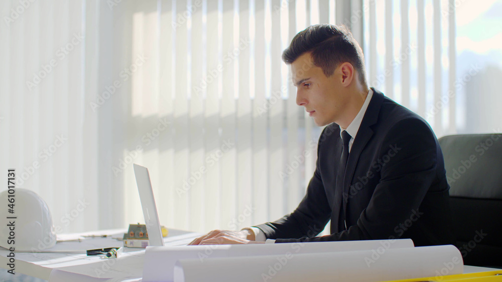 Confident and successful young businessman working on laptop in office