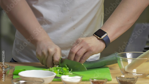 Cropped shot of chef slicing green leek in professional kitchen
