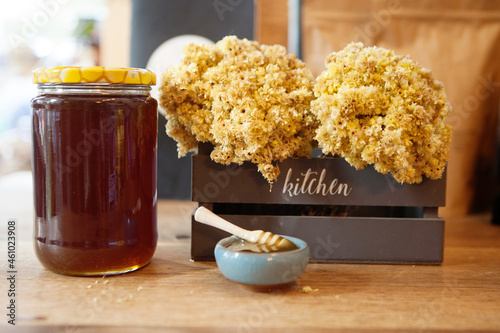 Honey dipper in a bowl of honey next to a jar of honey and mimosa flowers in a crate