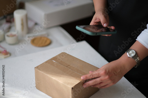 Small business owner standing at her shop arranges delivery through the application on a smartphone. online store seller entrepreneur packing package post shipping box preparing delivery parcel.